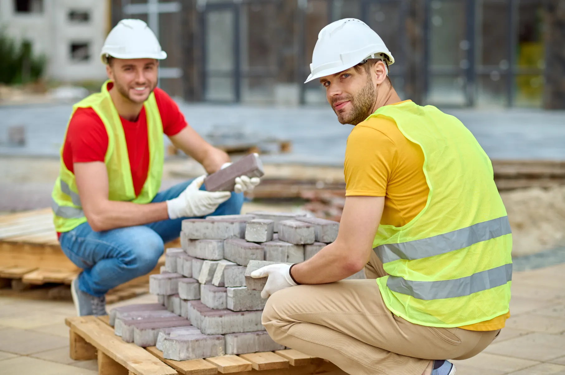 two workers stacking bricks looking camera